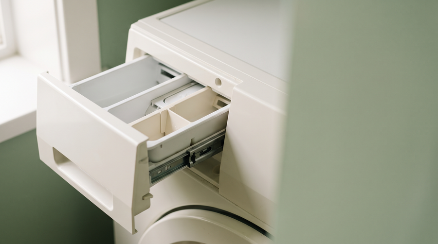 The open detergent drawer of a front-loading washing machine, compartments empty, in soft natural light